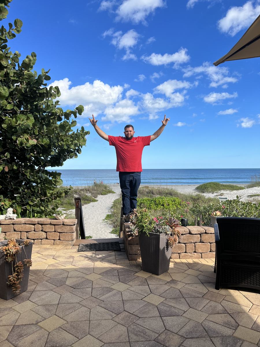 Mark Gabrielli with his arms raised on a beach walkway
