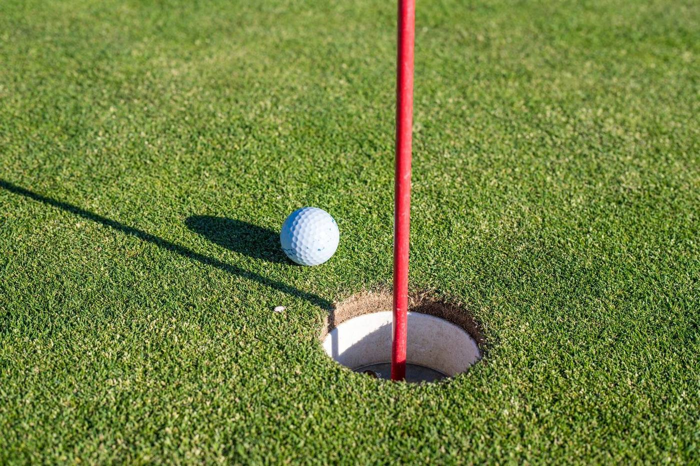 A close-up of a golf ball near a hole on a green with a red flagpole, symbolizing precision and sport.